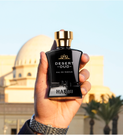 Hand holding a bottle of Desert Oud perfume with a building in the background.