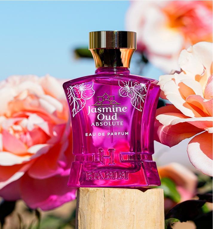 Pink perfume bottle with floral design, surrounded by blooming roses.