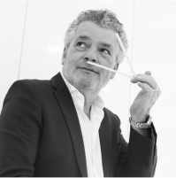 Man in suit holding sticks near nose, appearing thoughtful.