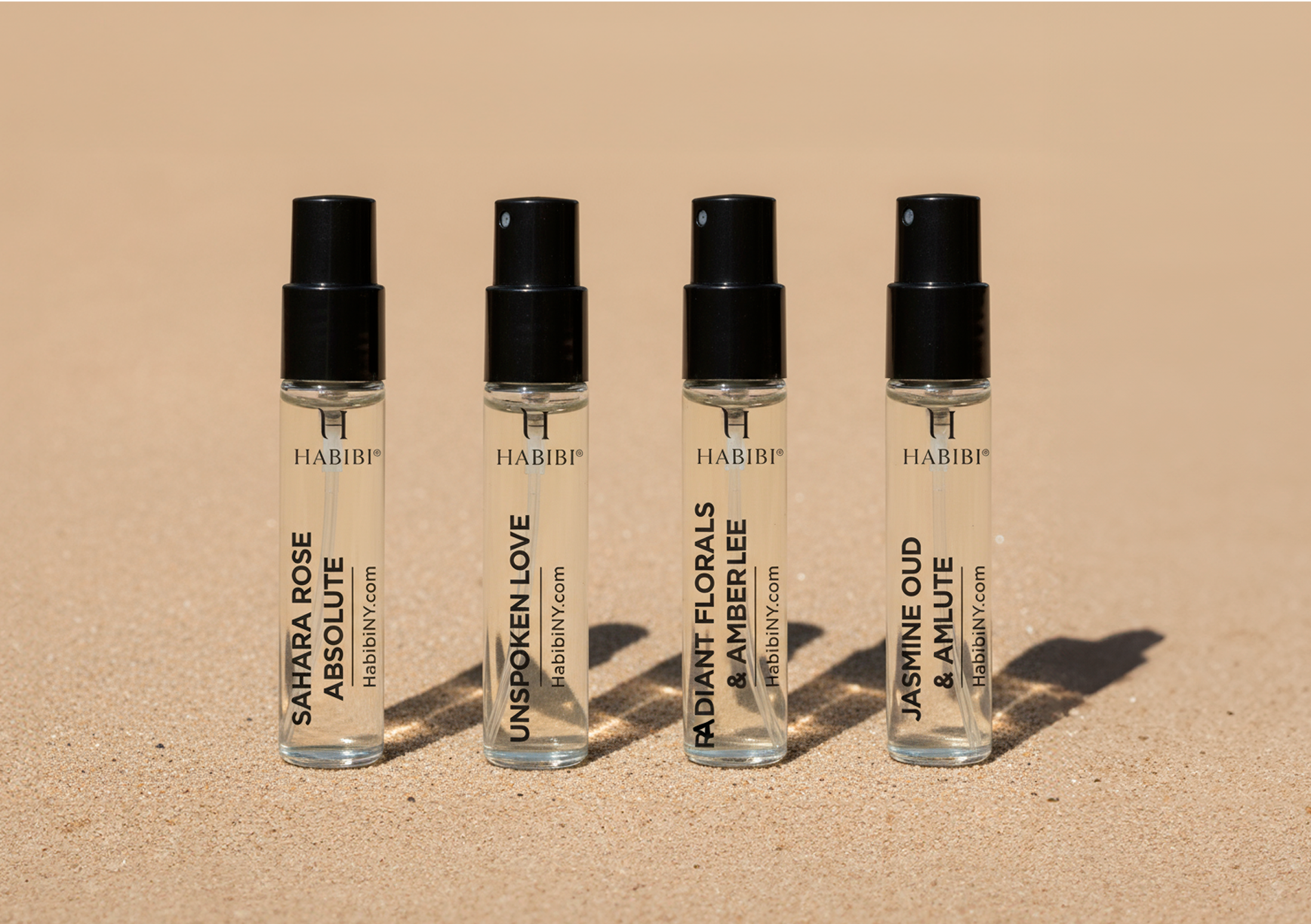 Four perfume vials with black caps on a beige background.