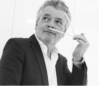 Man in suit holding two sticks near his nose, looking thoughtful.