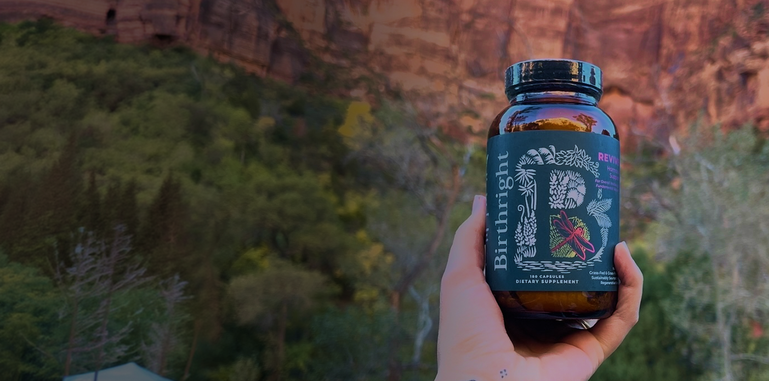 Lady holding a bottle of Birthright Revive with nature in the background