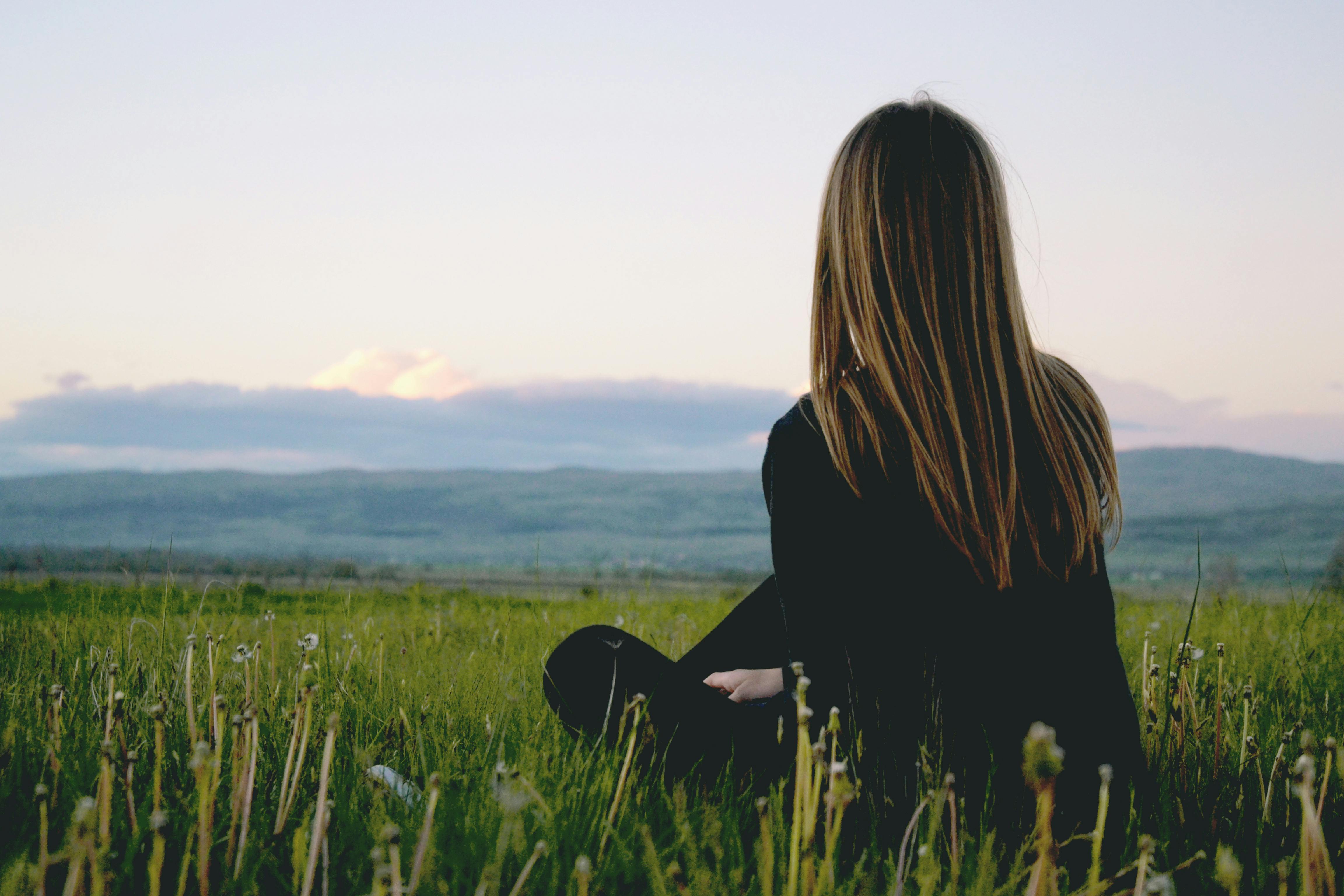 Person sitting in a field, facing the mountains at sunset.