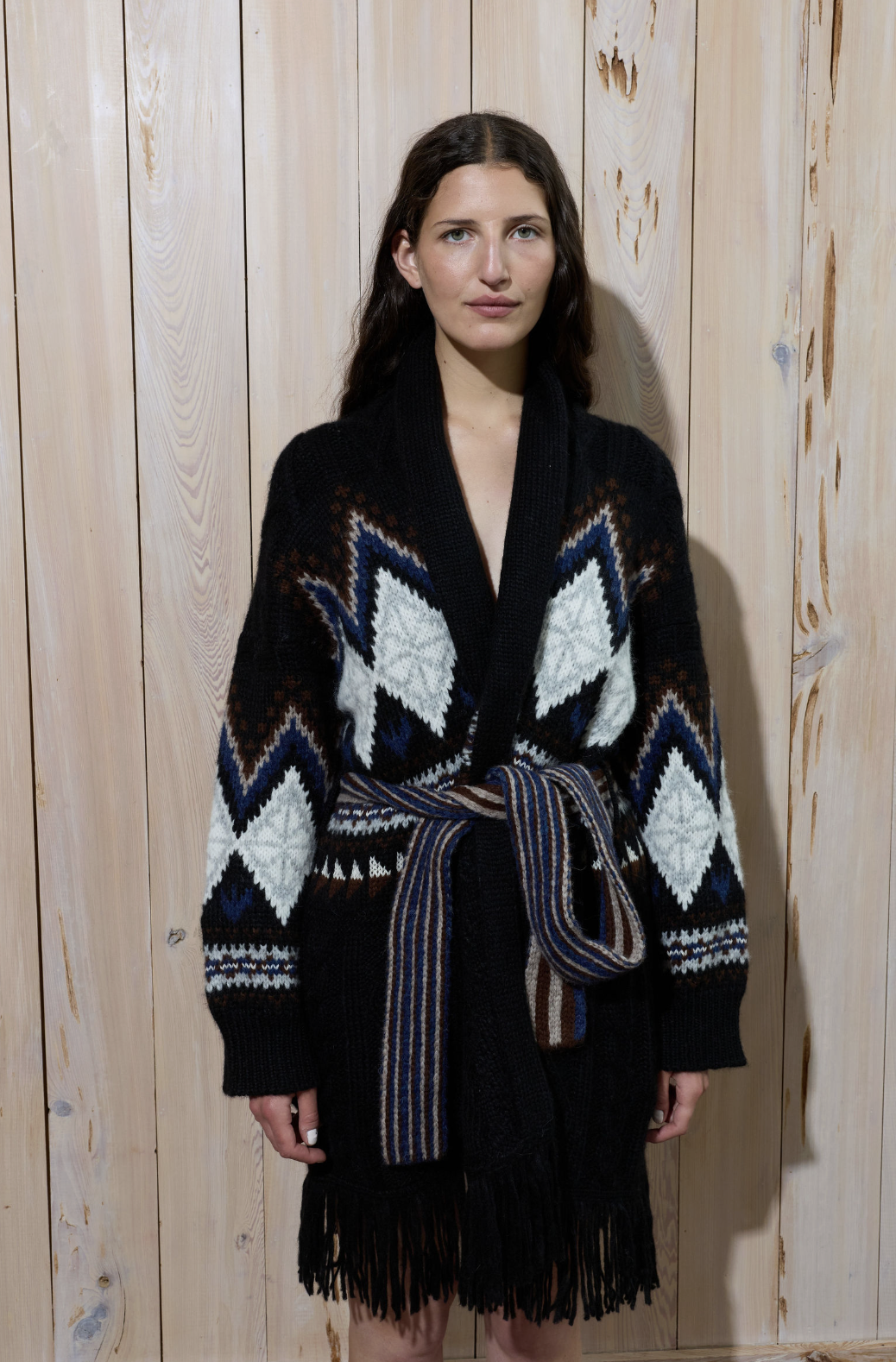 Person wearing a patterned knit cardigan against a wooden background.