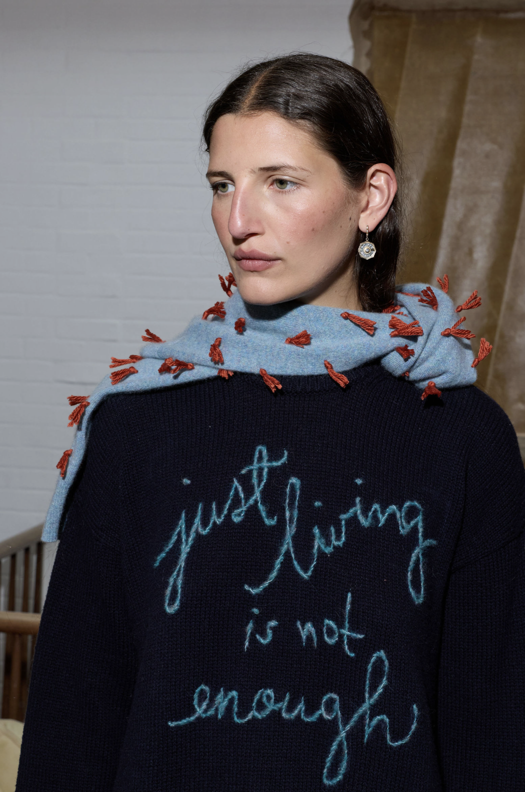 Person wearing a sweater with 'just living is not enough' text and a scarf.