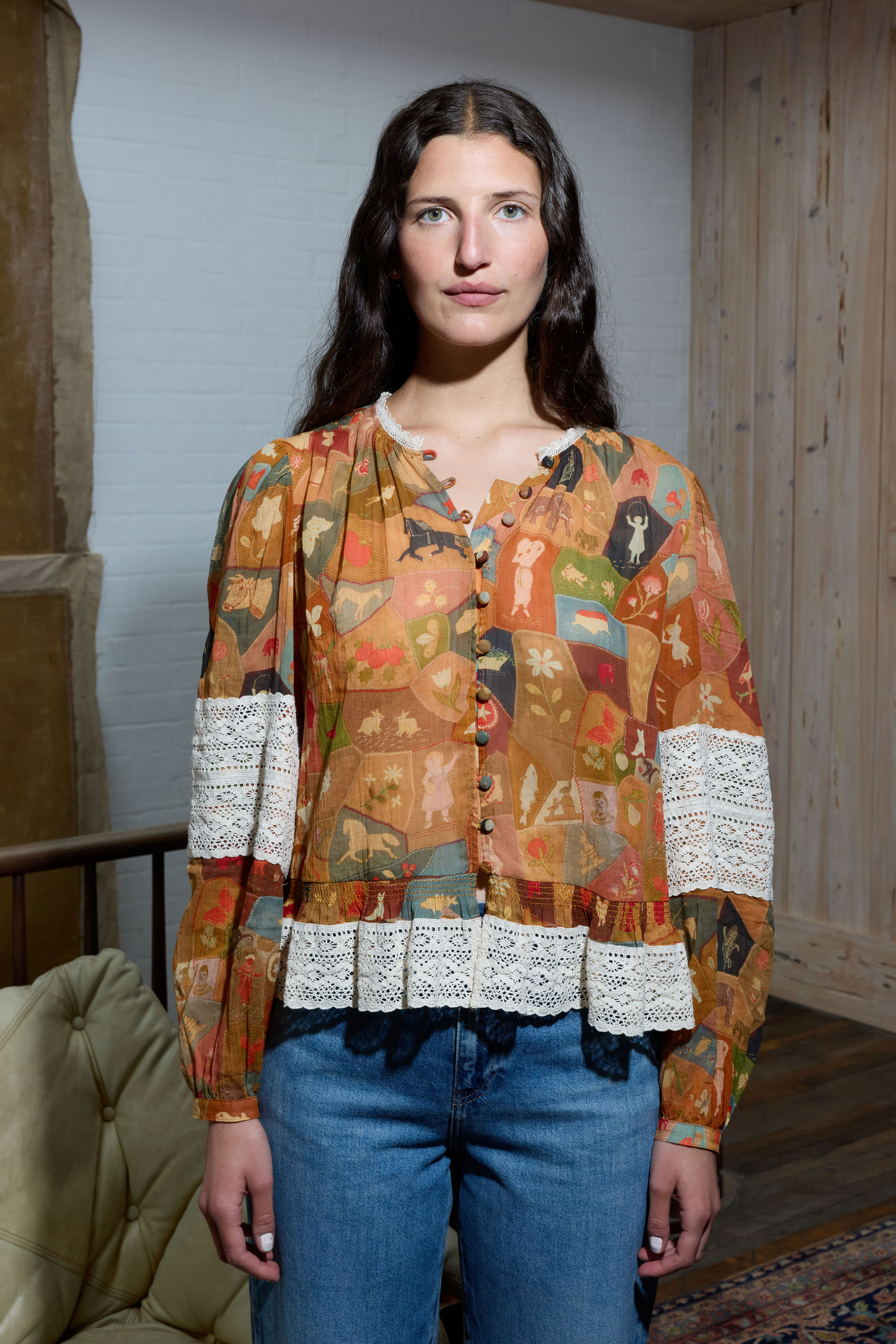 A person wearing a colorful patterned blouse and blue jeans indoors.