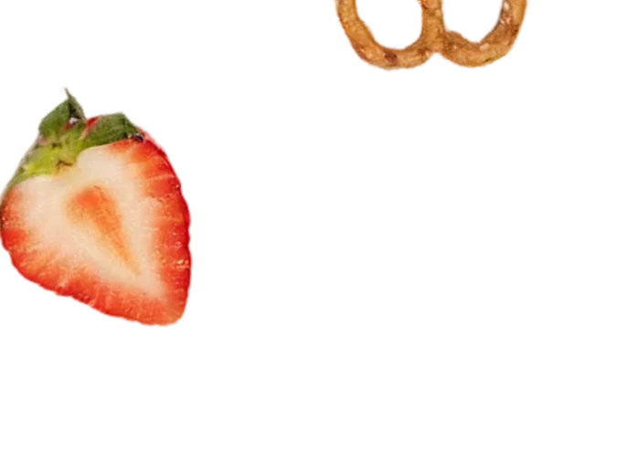 A close-up of a sliced strawberry and the top of a pretzel against a white background.