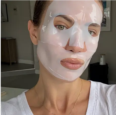 Person with a shiny facial sheet mask in a room.