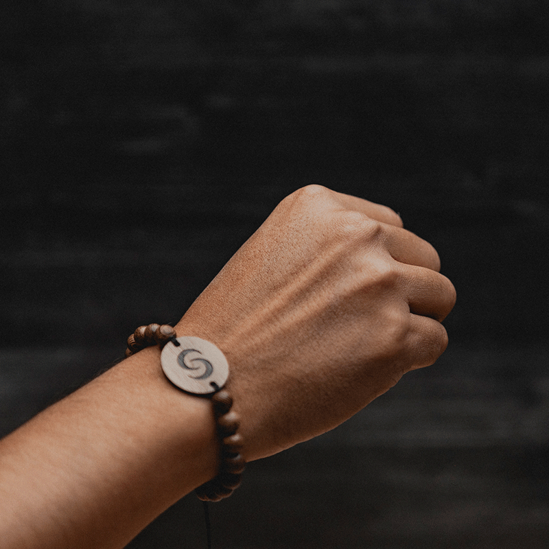 Hand wearing a beaded bracelet with a circular wooden pendant.