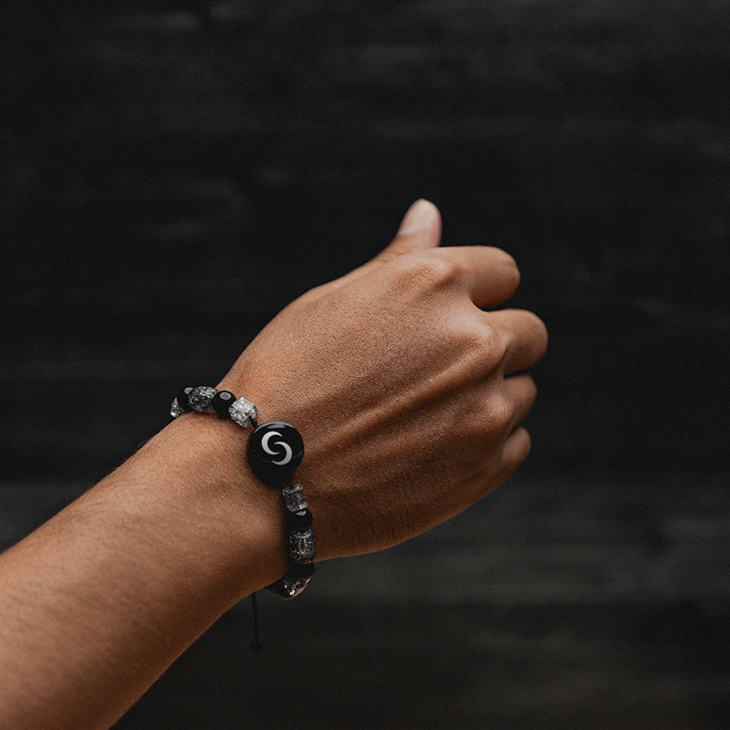 Hand wearing a black and gray bead bracelet with a circular charm.