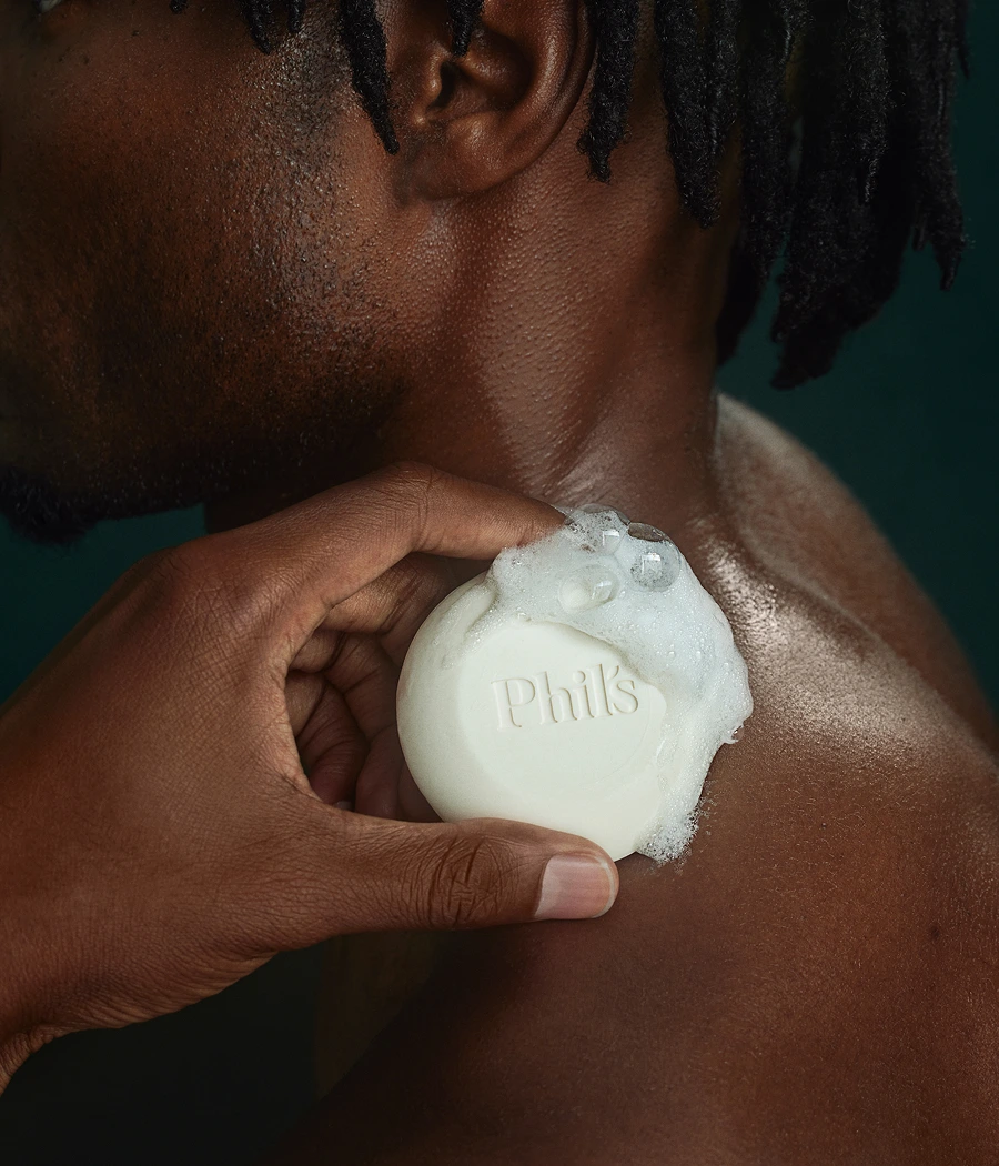 A person using a soap bar labeled 'Phil's' on their shoulder.