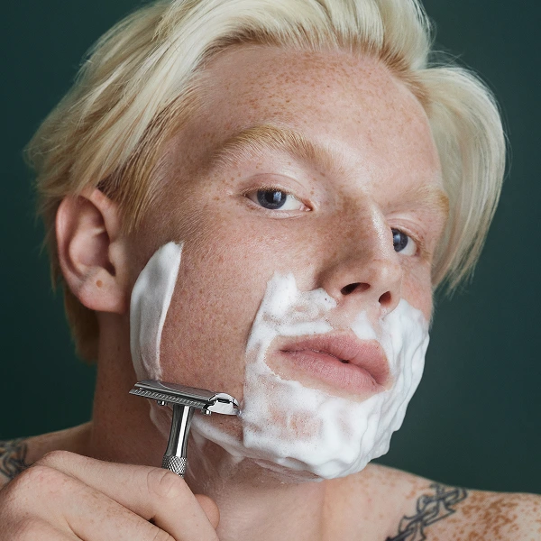 Person shaving with a safety razor, using shaving cream.