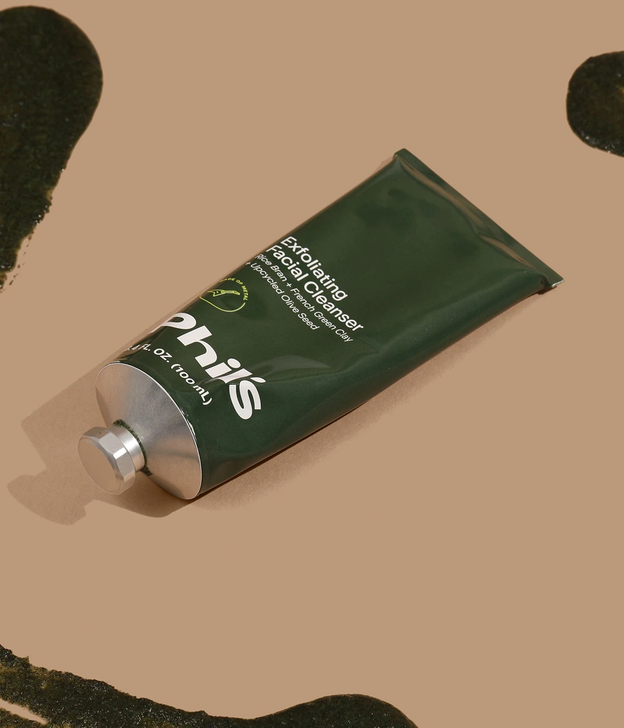 Green tube of exfoliating facial cleanser on a brown background.