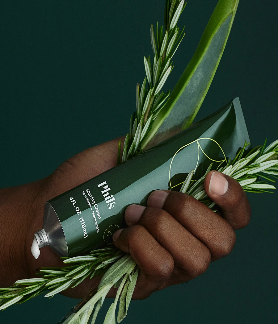 Hand holding a green tube of shaving cream with rosemary and aloe.