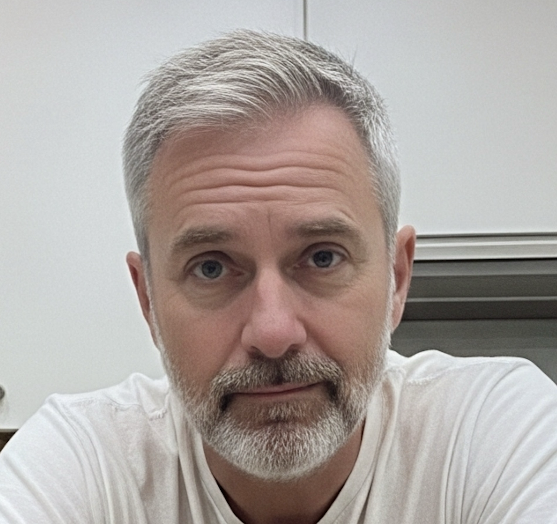 A man with gray hair and beard wearing a white shirt.