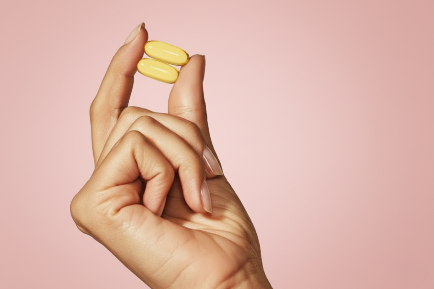 Hand holding two yellow pills against a pink background.