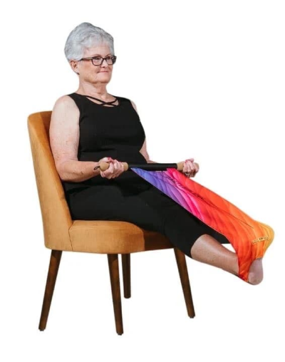 Woman seated in a chair using the CastleFlexx stretching strap to stretch her foot and hamstring