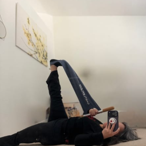 Customer photo of a woman lying on the floor stretching her legs up with a CastleFlexx strap