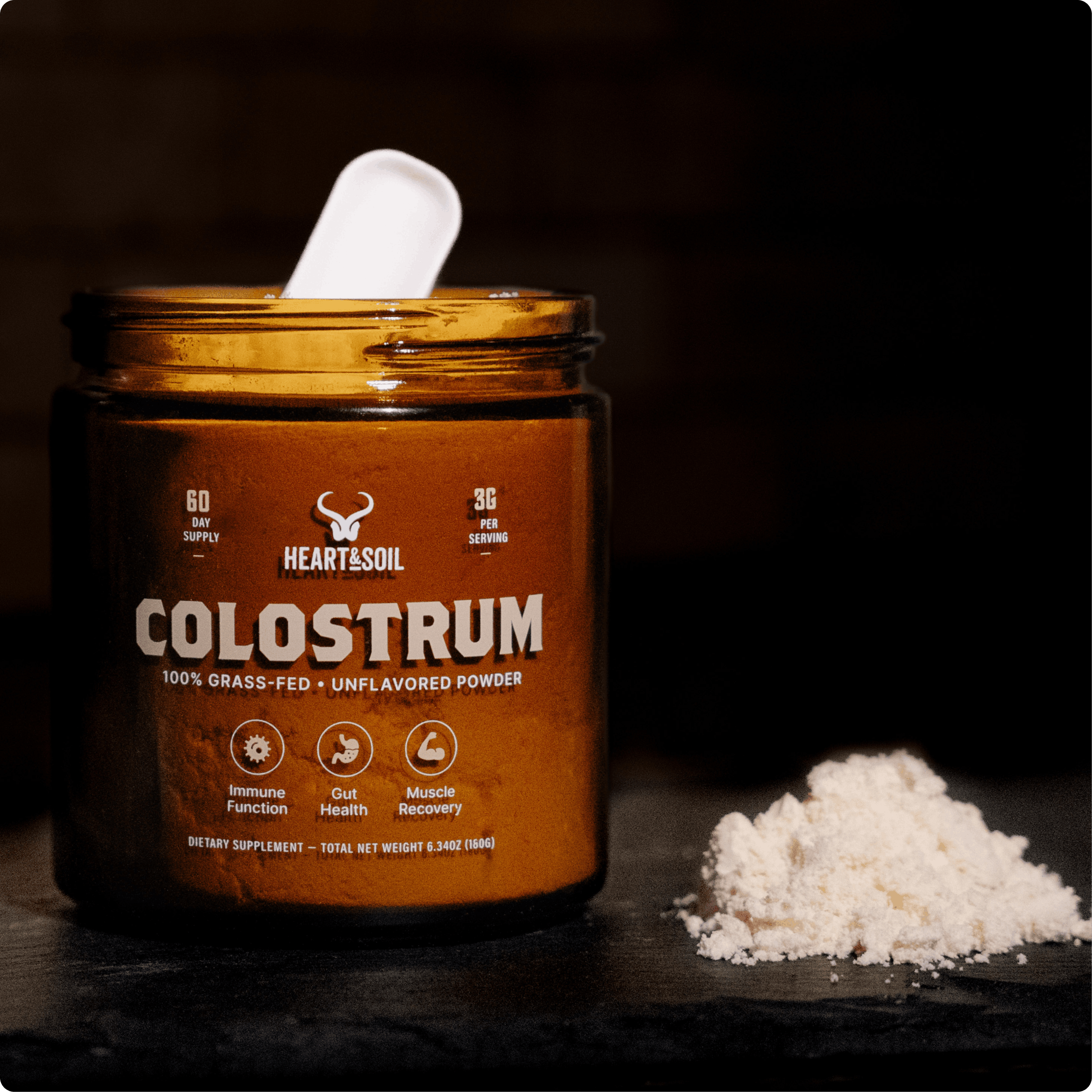 A jar of Heart & Soil Colostrum powder sits on a dark surface with a scoop and a pile of powder.