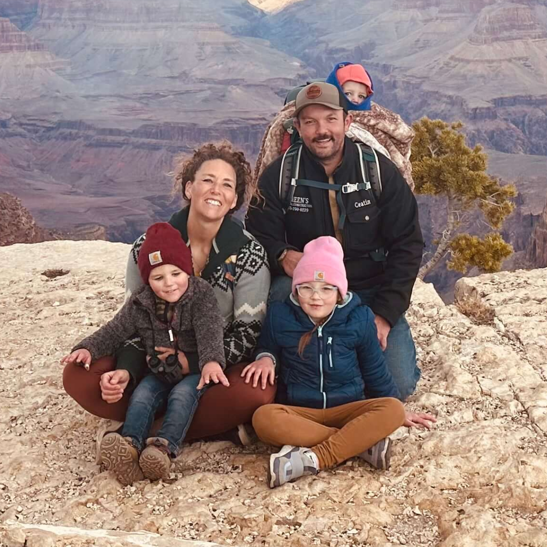 A family of five posing for a photo on a rocky ledge overlooking a large canyon.