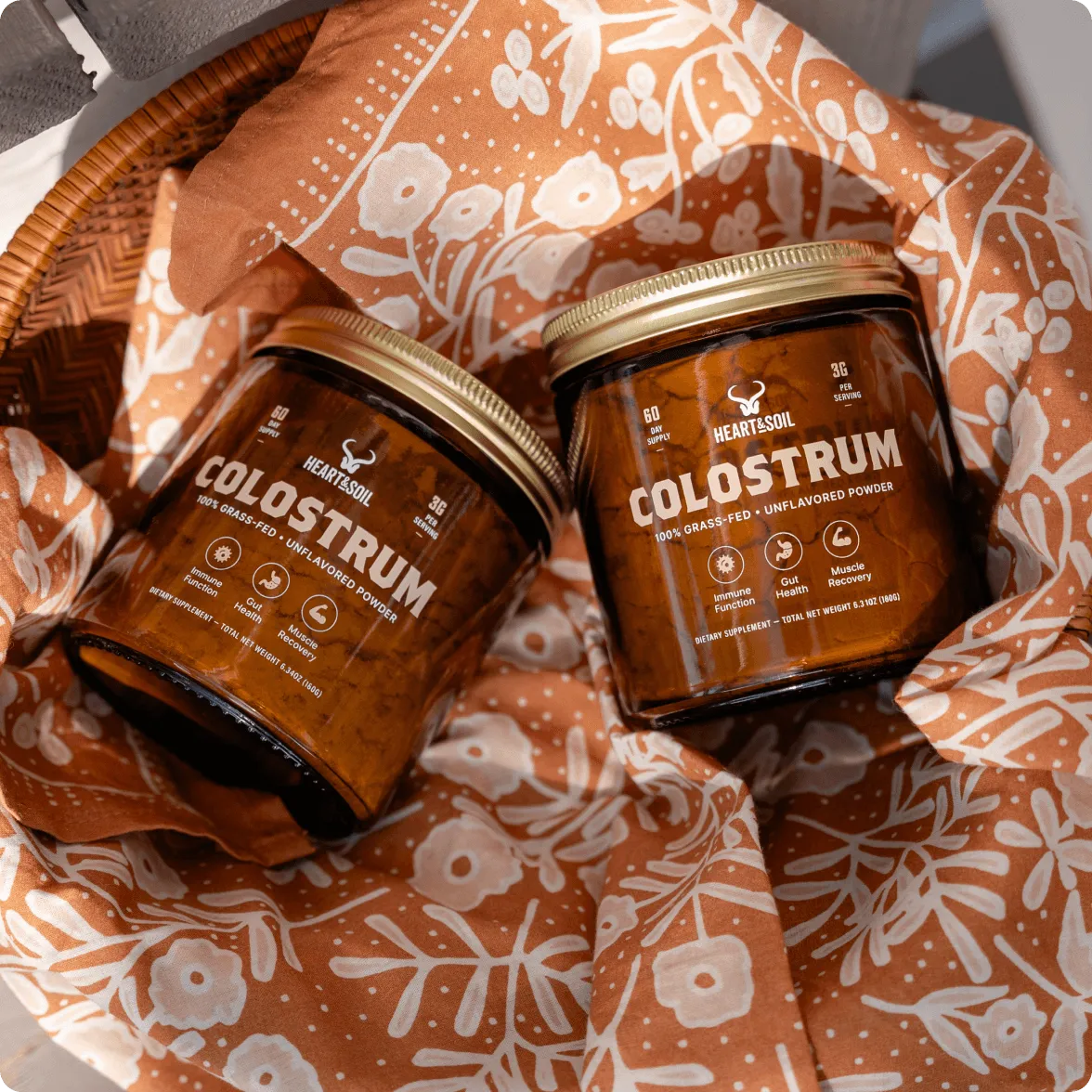 An overhead shot of two jars of Heart & Soil Colostrum powder in a basket with a patterned cloth.