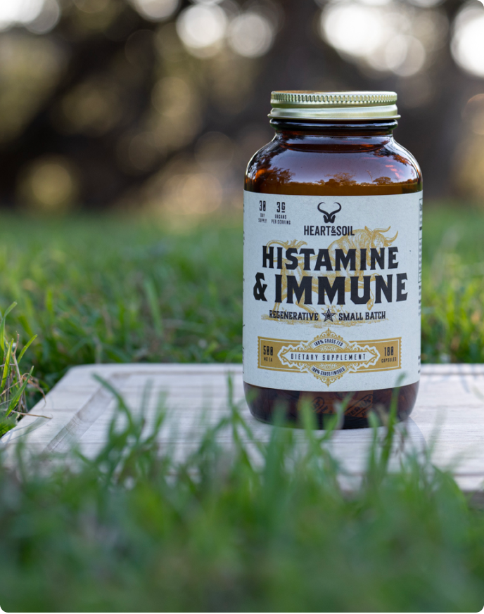 A bottle of Heart & Soil Histamine & Immune supplement sits on a wooden board in the grass.