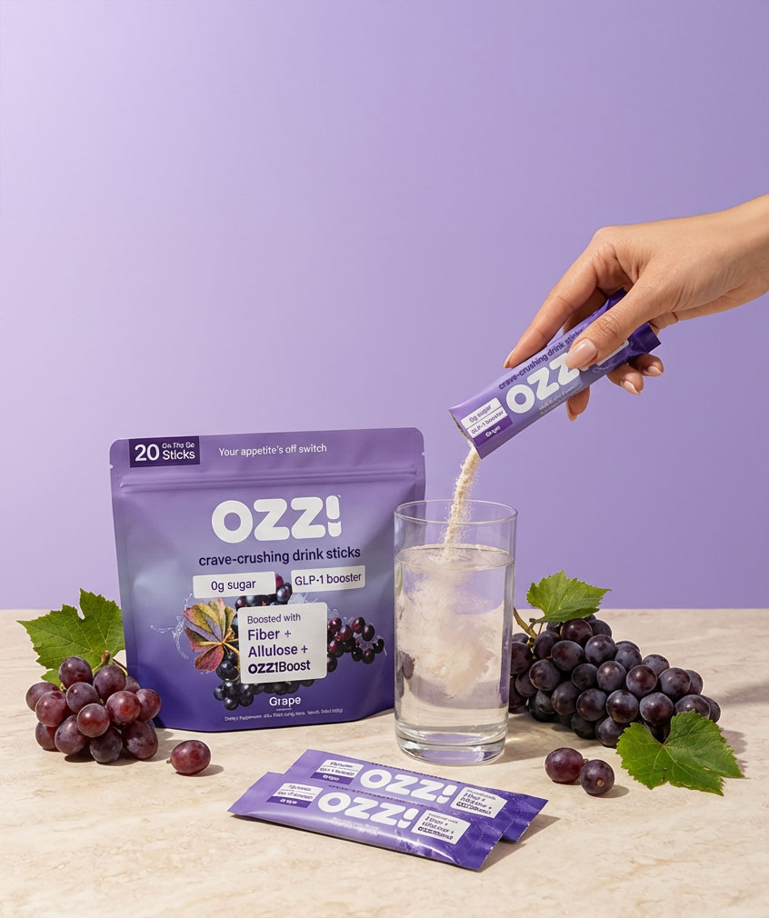 Hand pouring powder from stick into glass, next to grape drink product packaging.