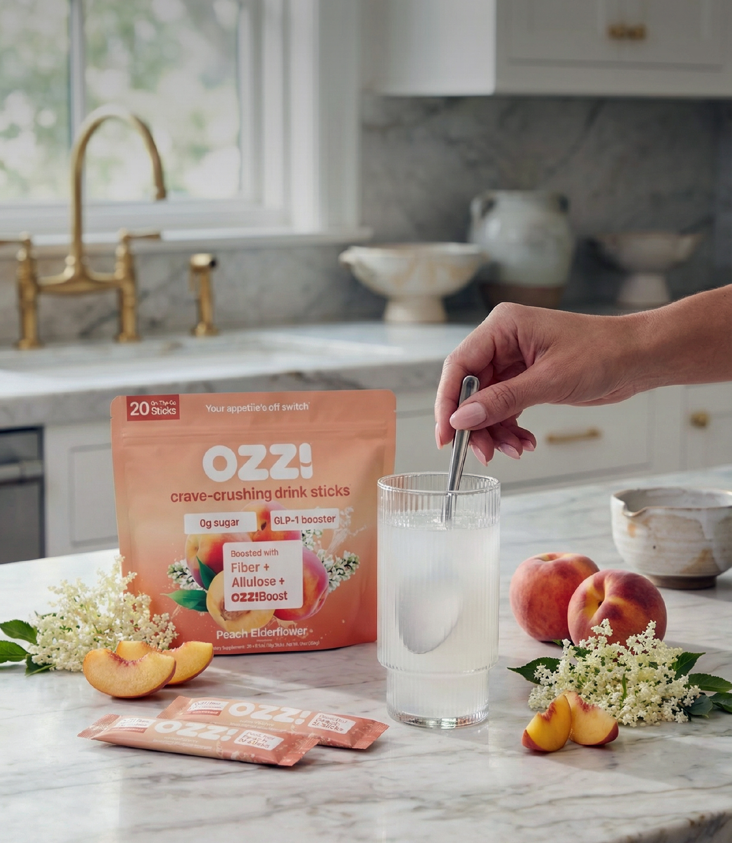 A person stirs a glass of OZZ! drink mix next to peaches and elderflowers on a countertop.