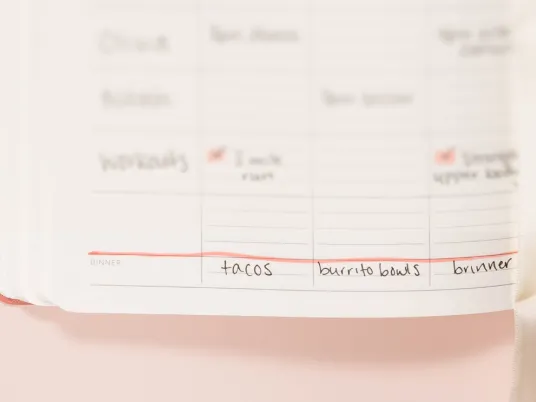 A close-up of a handwritten weekly planner showing dinner ideas like tacos and burrito bowls.