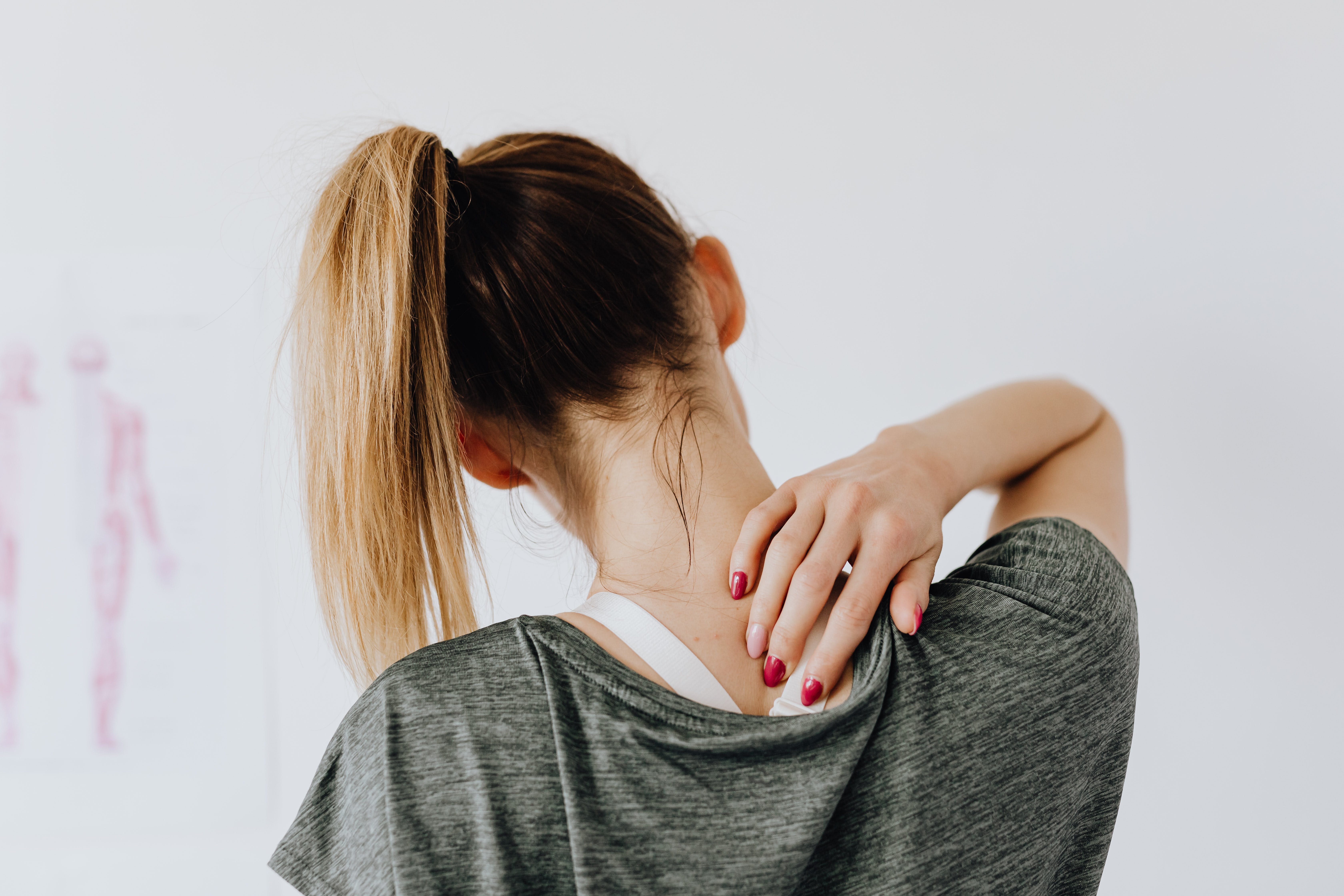 Person with ponytail touching their neck, wearing a gray shirt.