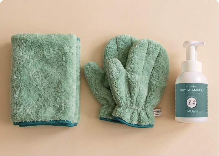 A fluffy green towel and mitten are laid out next to a bottle of foaming dry shampoo.