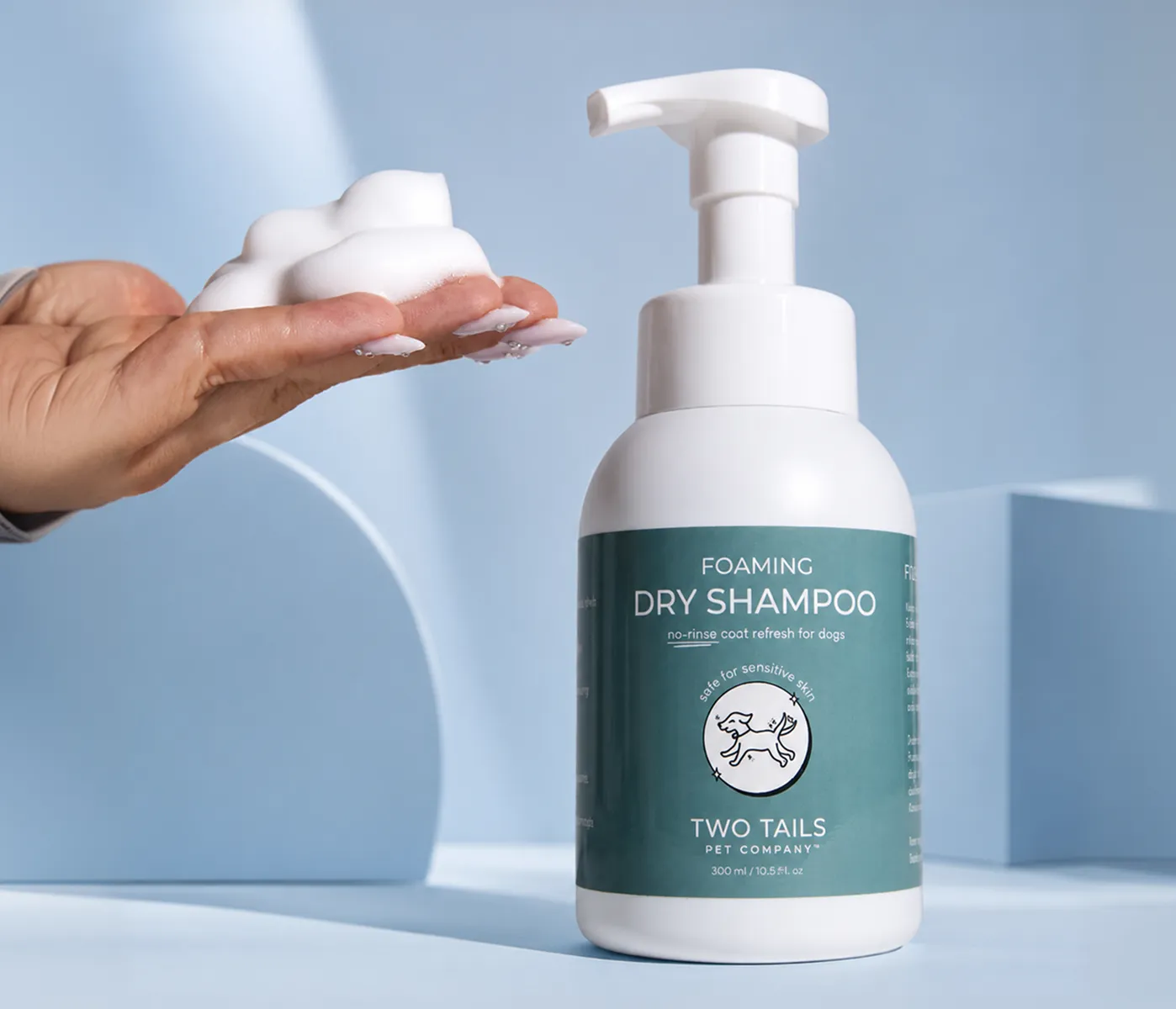 A bottle of Two Tails Pet Company Foaming Dry Shampoo next to a hand holding a dollop of foam.