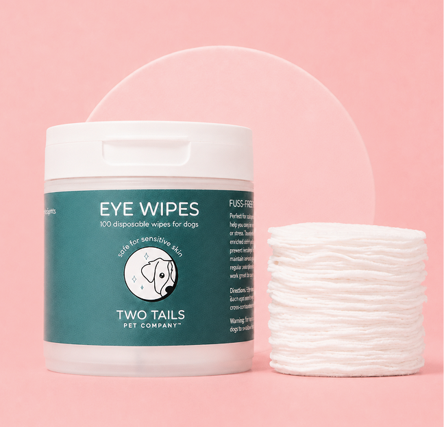A container of Two Tails Pet Company eye wipes for dogs next to a stack of round wipes.