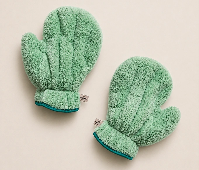 Two fluffy, green, textured microfiber mittens on a cream-colored background.