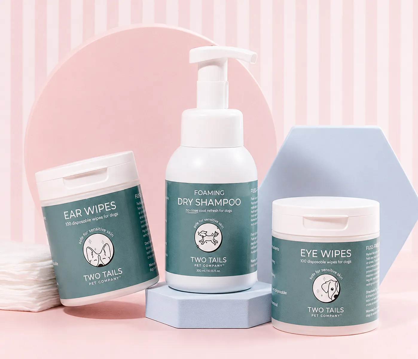 Two Tails Pet Company foaming dry shampoo, ear wipes, and eye wipes for dogs on geometric blocks.