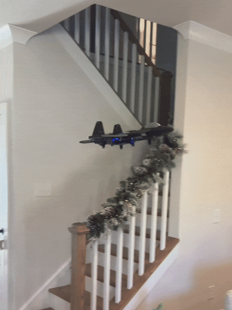 A small drone flying indoors near a stairway with holiday garland.