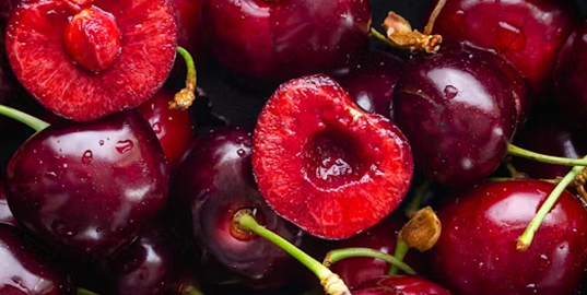 A close-up of ripe, dark red cherries, with a few cut in half showing the flesh and pits.