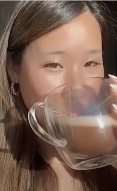 A close-up of a woman with long hair drinking from a clear glass mug.