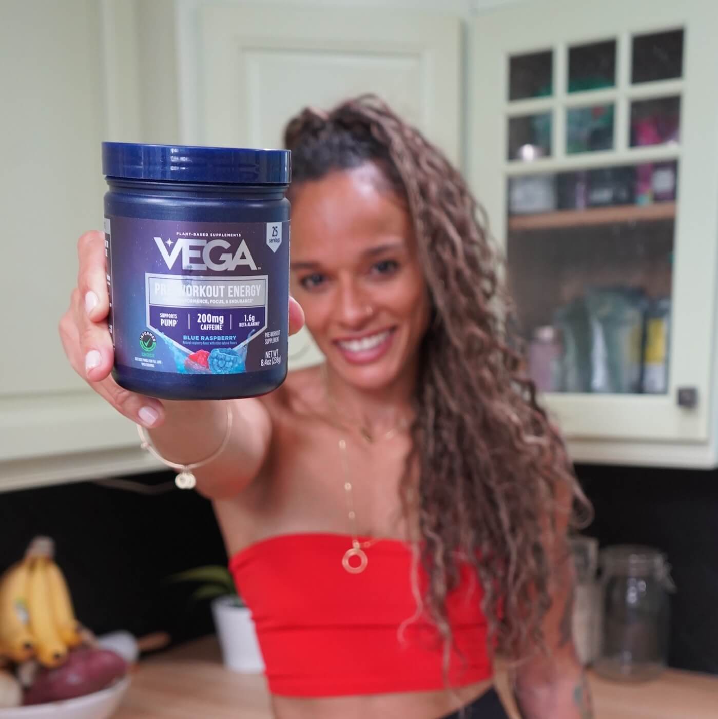 Person holding a container of Vega pre-workout energy in a kitchen.