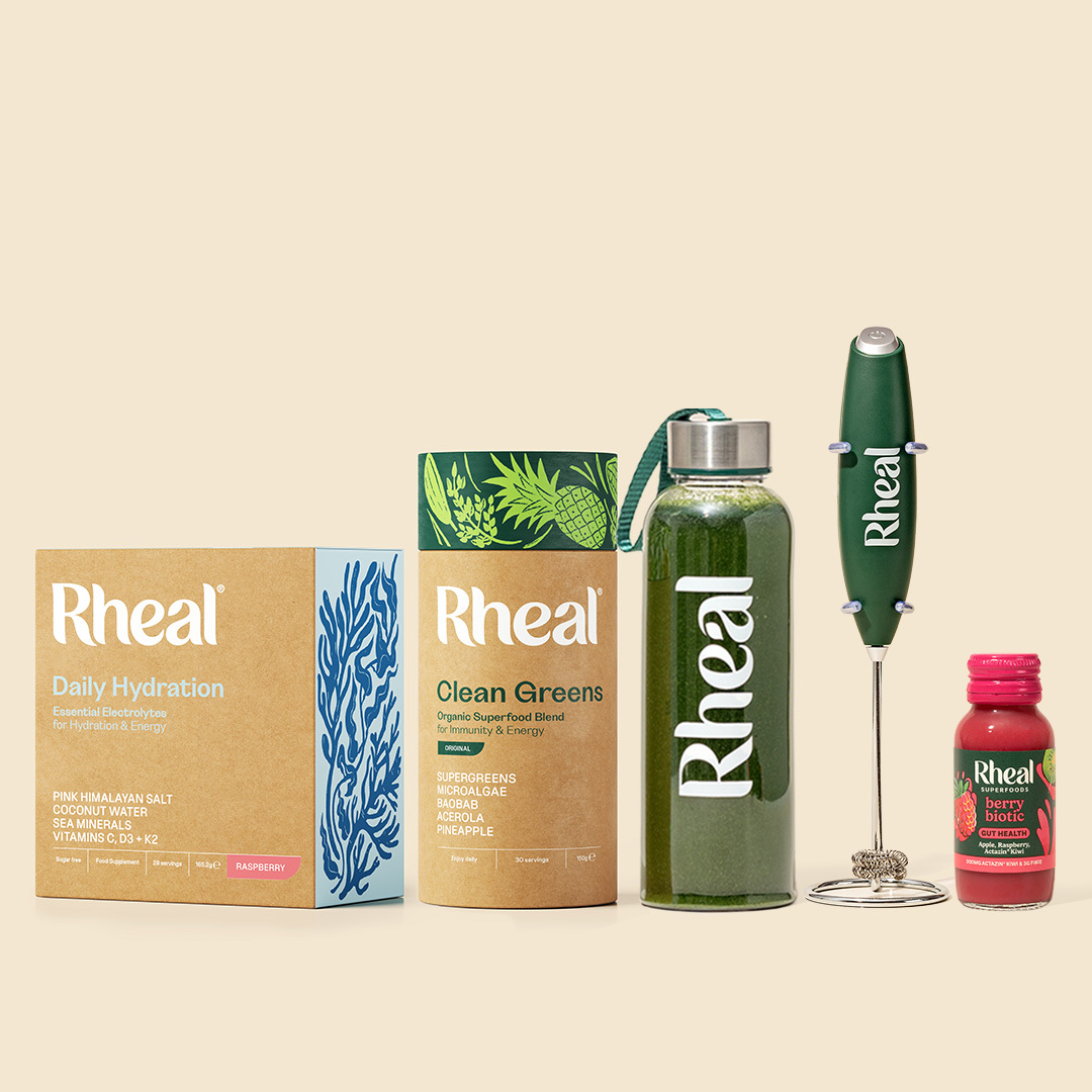 A collection of Rheal brand nutritional products, including powders, a drink, a small bottle, and a frother.