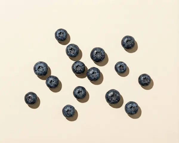 A top-down photo of several blueberries scattered across a light-colored surface with direct lighting.