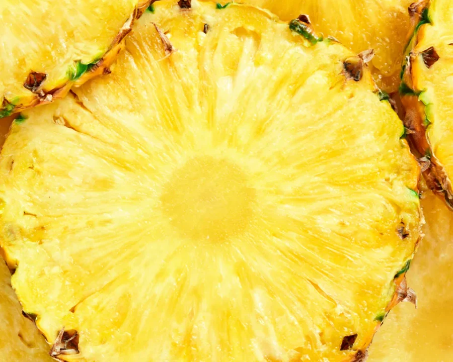 A close-up shot of a bright yellow, round slice of pineapple with its rind still on.