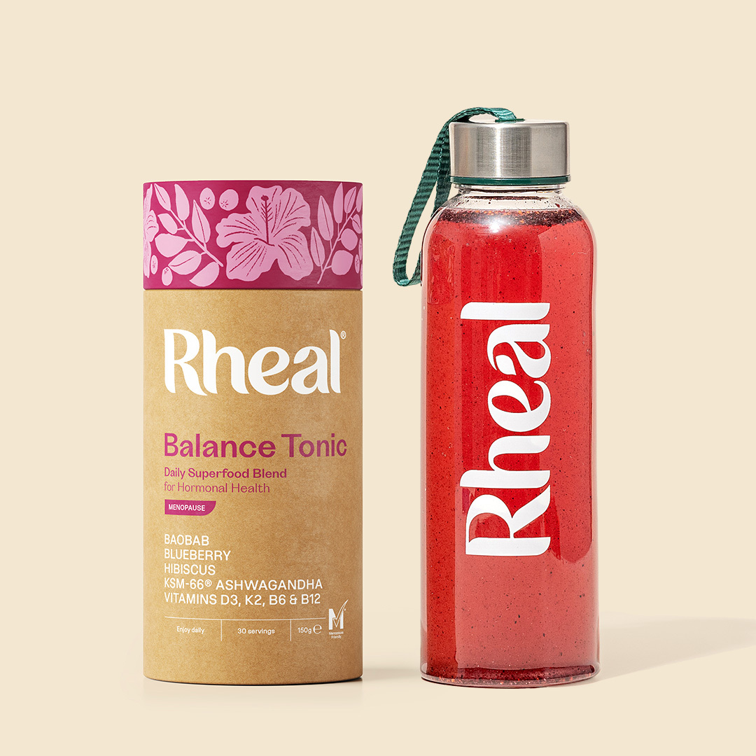 A tube of Rheal Balance Tonic next to a branded glass bottle filled with a red beverage.