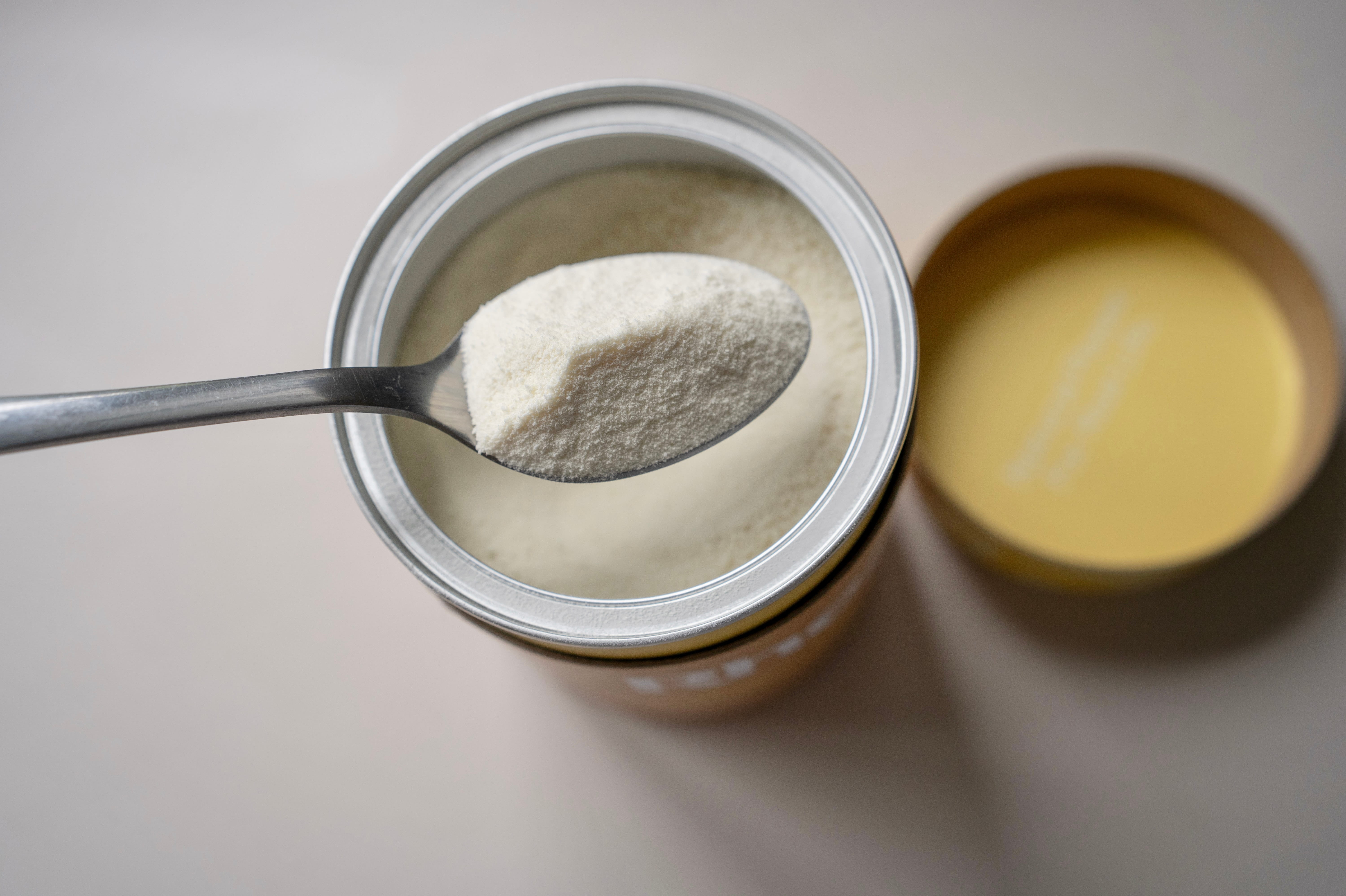A top-down view of a spoon holding white powder over an open canister.