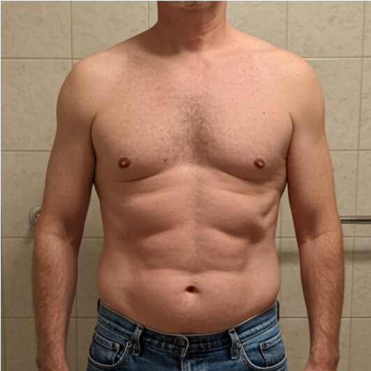 Shirtless man in jeans standing against a tiled wall.