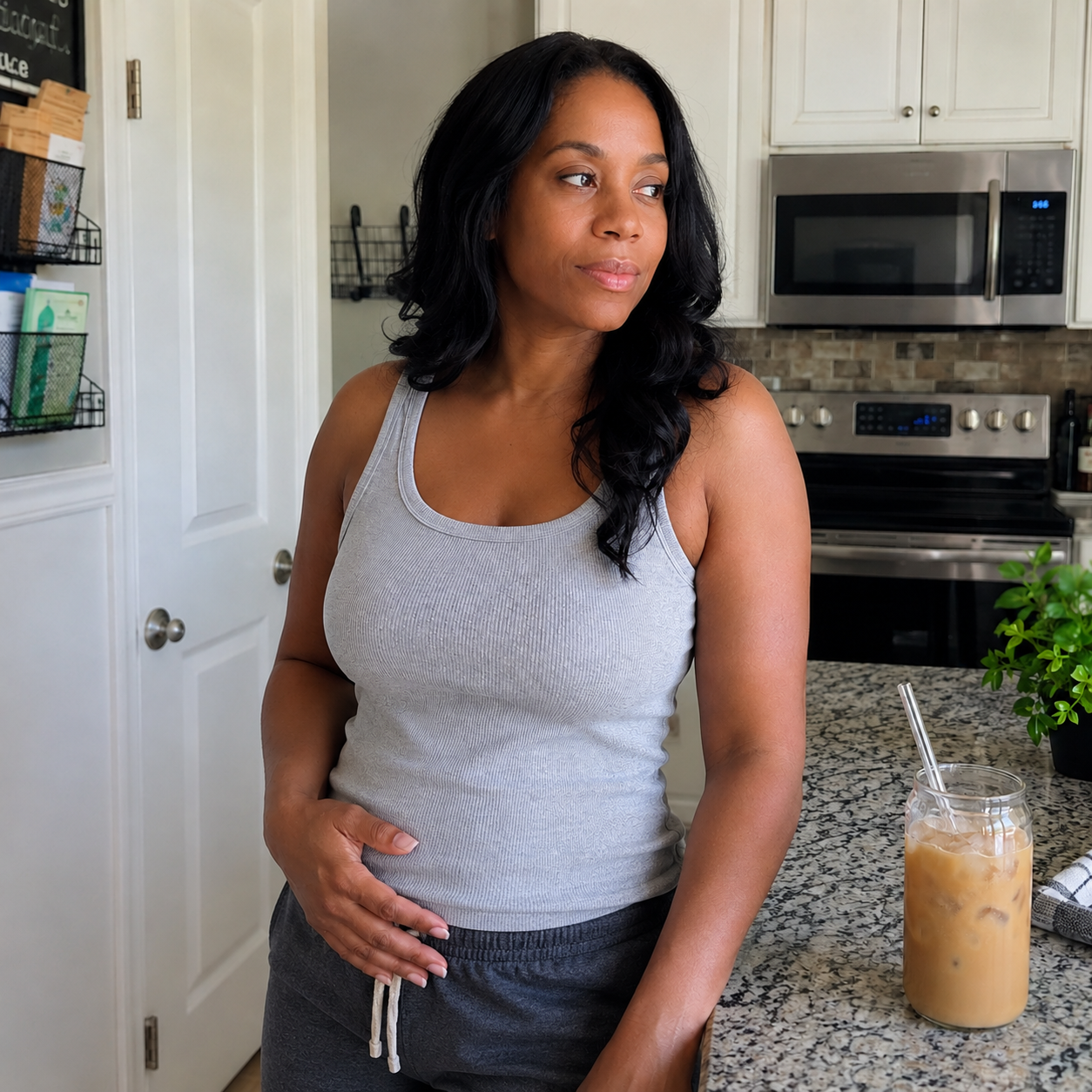 A woman in a grey tank top stands in a kitchen, looking to her right.