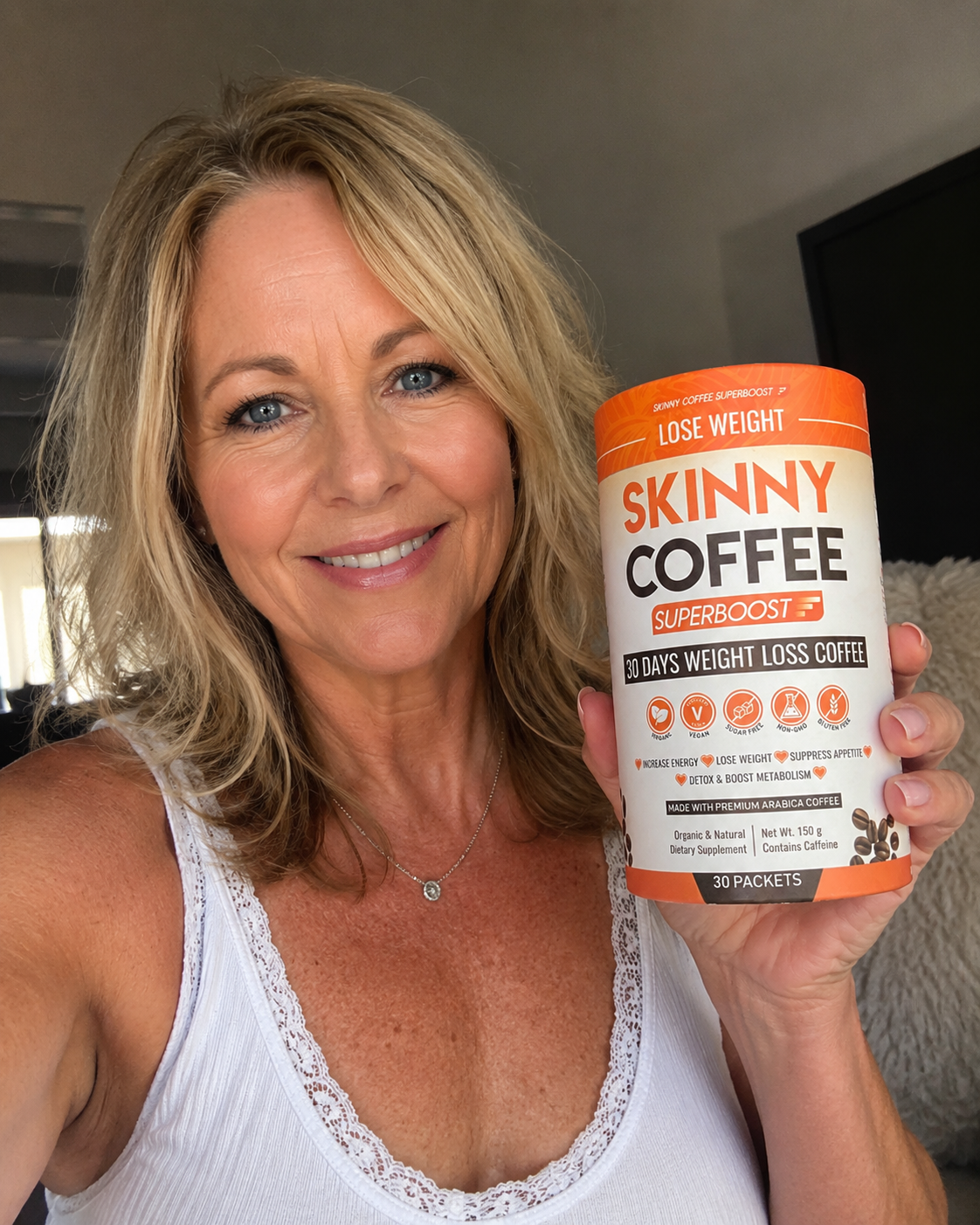 A smiling blonde woman in a white tank top holds a container of Skinny Coffee Superboost.