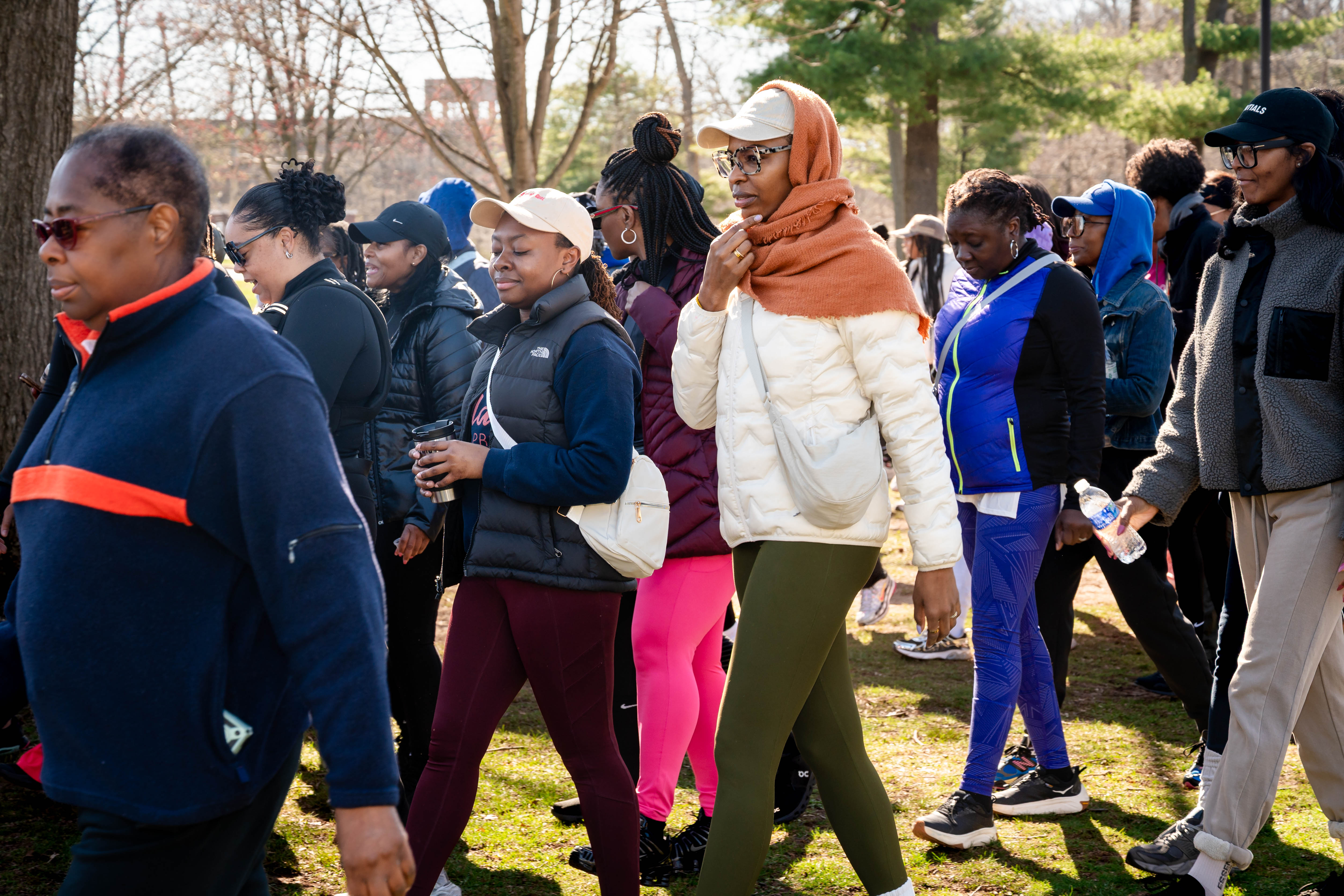 A group of predominantly Black people walk together outdoors through a park on a sunny day.