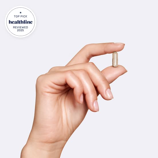 Hand holding a small capsule against a plain background.