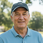 A smiling older man wearing a baseball cap and a light blue polo shirt outdoors.